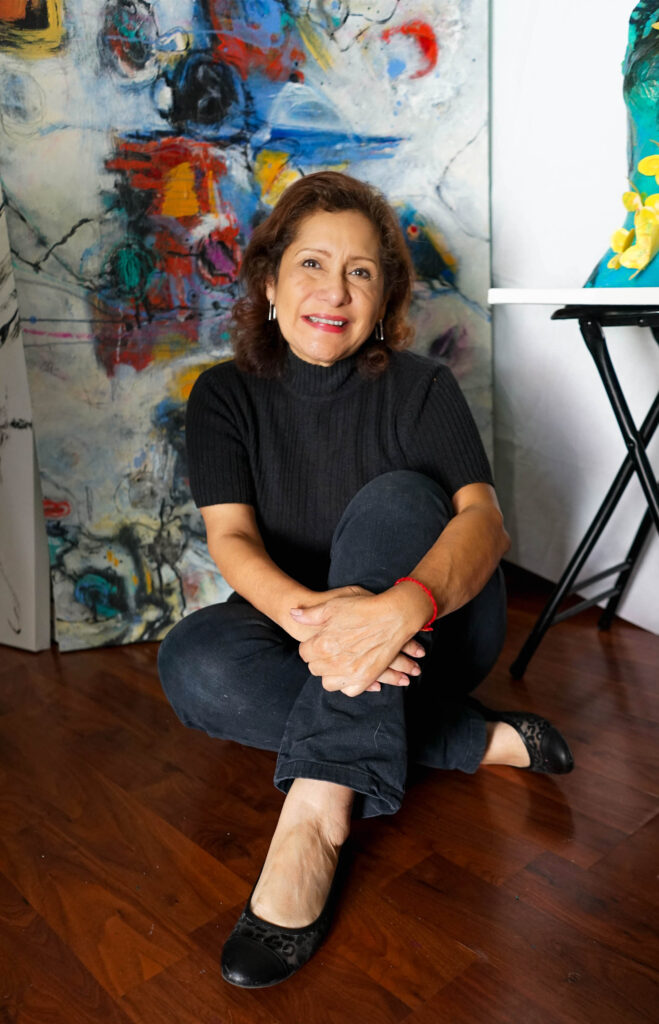 Eumelia Castro smiling while seating on the floor at her studio